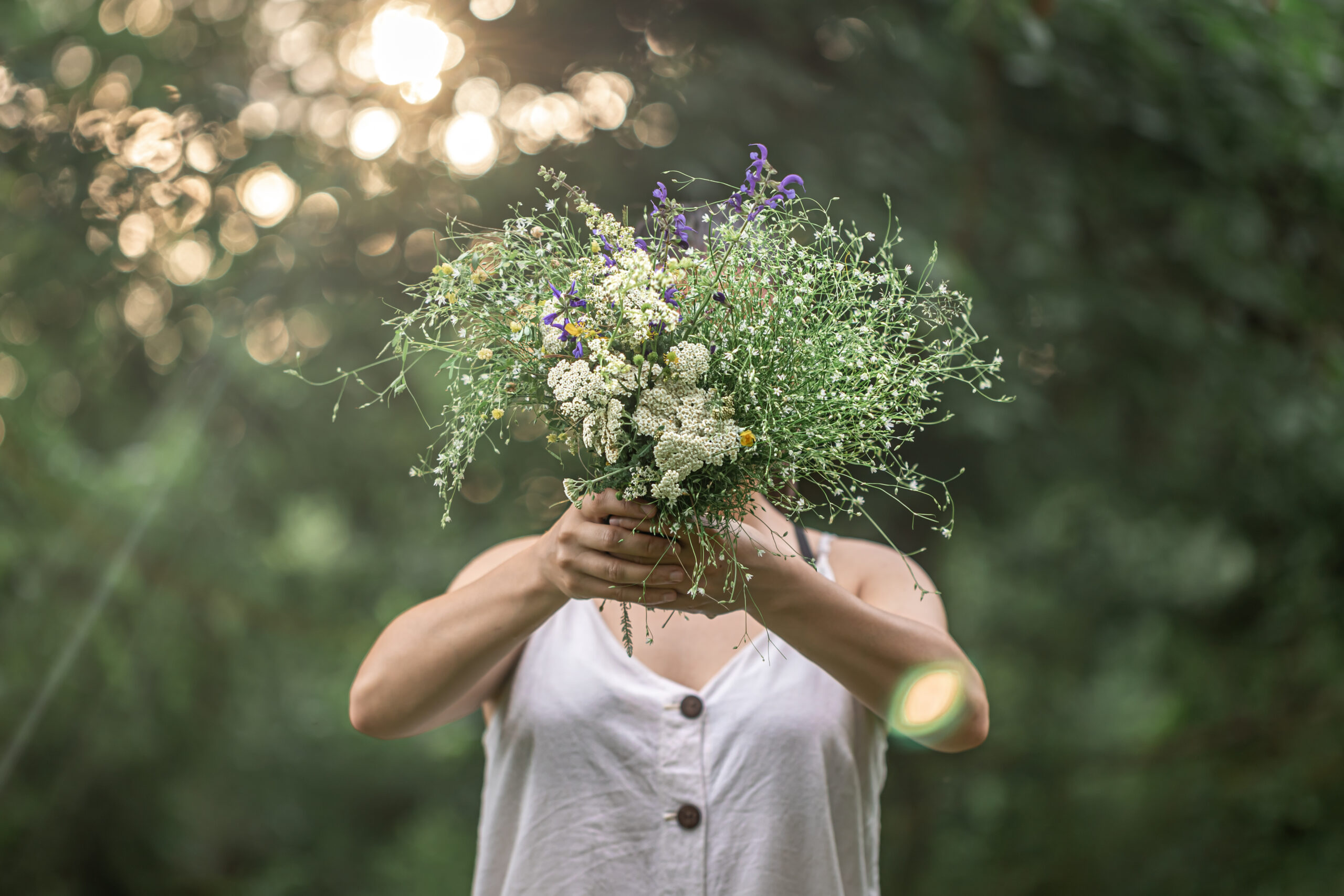 Girl holding a bouquet of flowers on a blurred background with bokeh. A bouquet of wild flowers in the hands of a girl on a blurred background in the forest.